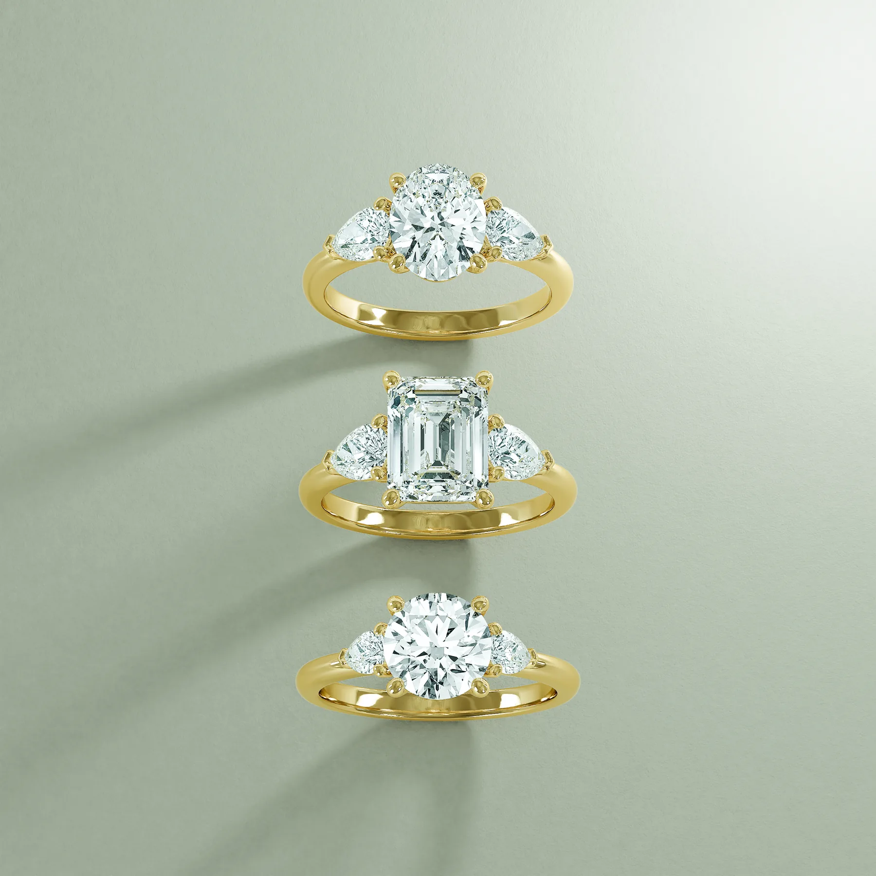 Three-stone engagement rings in yellow gold with oval, emerald-cut and round centers and pear-shaped side stones